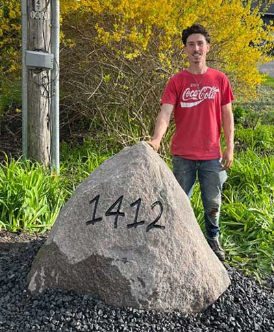 Garrit standing beside a large rock that he has engraved a number